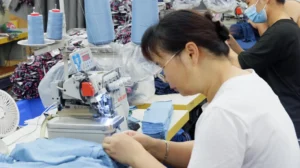 Close-up shot of a professional factory worker precisely sewing organic cotton garments, demonstrating the high-quality craftsmanship of an eco friendly custom clothing supplier.