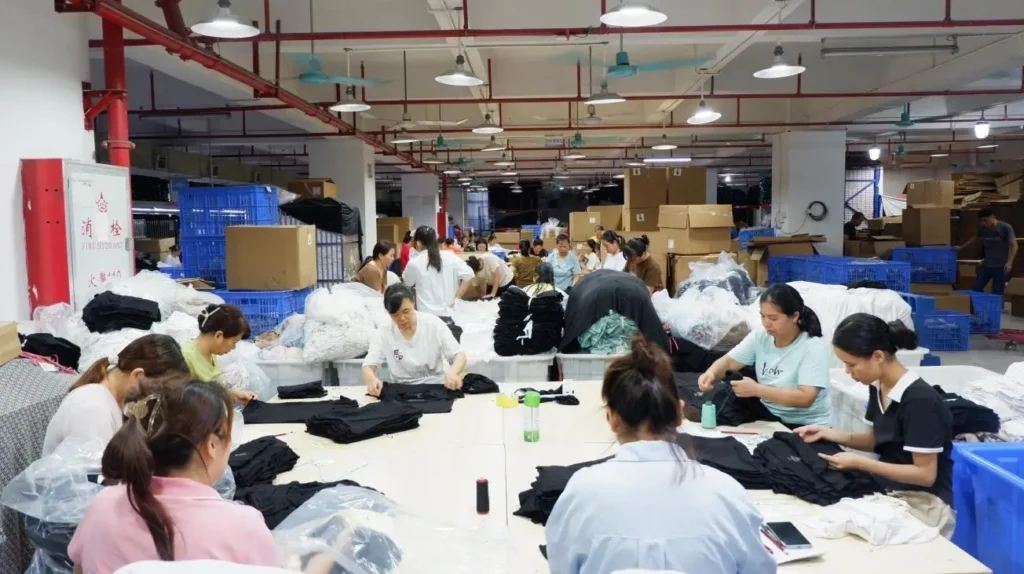 Workers performing quality control and packaging for bulk T-shirt orders on the factory floor, ensuring strict B2B garment manufacturing standards.