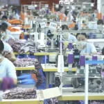 Sewing workers at custom apparel factory production line stitching garments